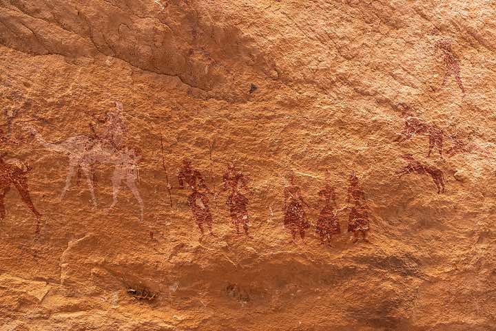 Rock painting depicting a rider on a camel, human figures and a hunting scene (upper right) with a human figure, two dogs chasing a goat, Kozen rock art site, Tibesti region