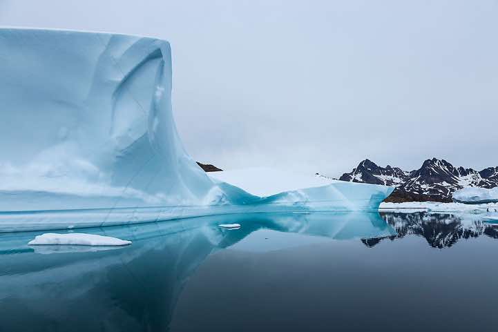 Iceberg and mountains reflecting in water, Ammassalik Island