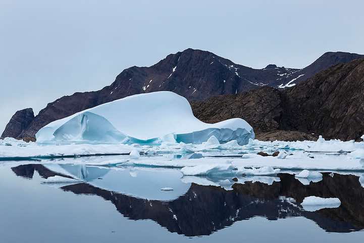 Iceberg and mountains reflecting in water, Ammassalik Island