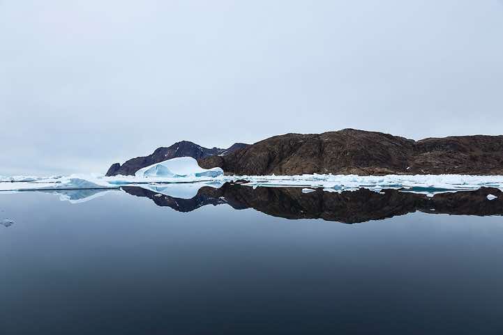 Iceberg and mountains reflecting in water, Ammassalik Island