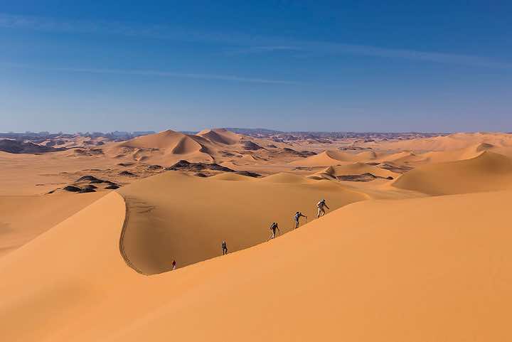 Walking up a tall sand dune, southern Oued In Tehak, Tadrart region, Tassili n ́Ajjer National Park, Sahara, North Africa