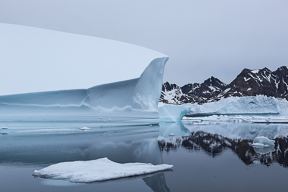 Large iceberg and mountains reflecting in water, Ammassalik Island, East Greenland